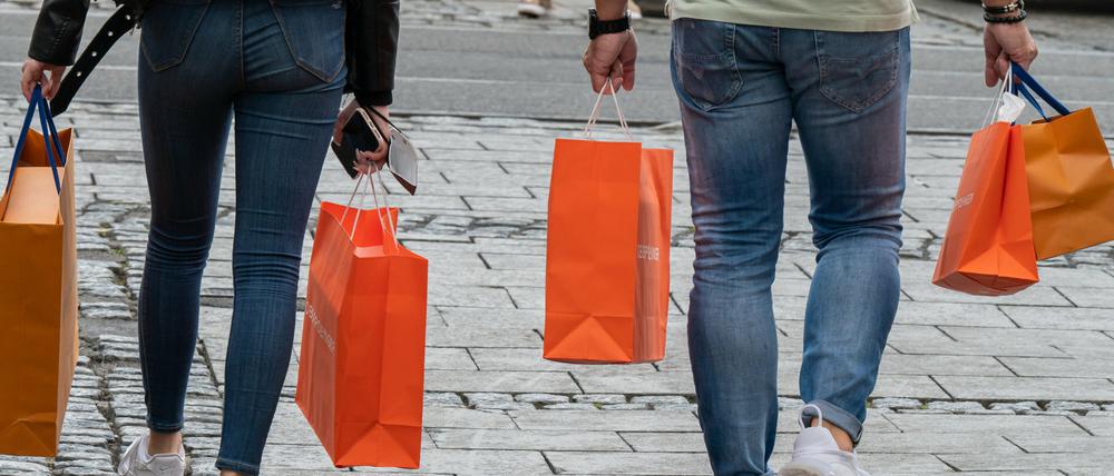 Passanten mit Einkaufstüten gehen bei Nieselwetter durch die Fußgängerzone in der Innenstadt. 