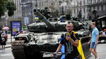 Ein Mann in einem T-Shirt mit dem Symbol des ukrainischen Wappens und der ukrainischen Flagge telefoniert in der Nähe der zerstörten Ausrüstung der russischen Armee in Kiew.
