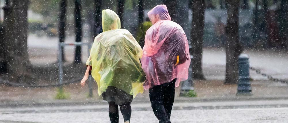 Passanten mit Plastik-Regenschutz gehen nahe des Brandenburger Tors durch den Regen. 