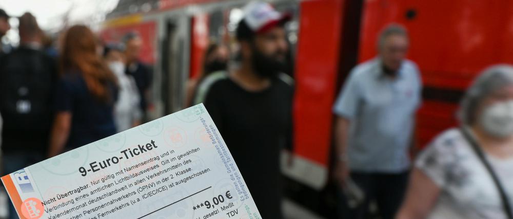 Ein 9-Euro-Ticket für Juli 2022 wird am Hauptbahnhof hochgehalten, während Zugreisende aus einer Regionalbahn aussteigen.