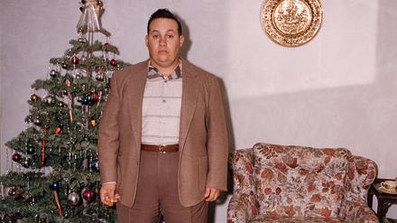 Mann steht neben einem Weihnachtsbaum.