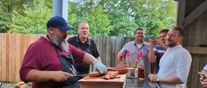 Grillweltmeister Oliver Sievers (l.) schneidet den gegrillten Schweinebauch an und gibt dabei Tipps für die richtige Zubereitung.