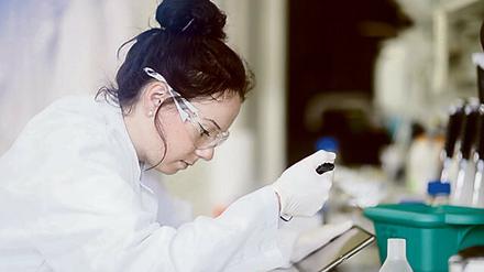 Eine junge Wissenschaftlerin pipettiert im Labor und hält dabei einen Tablett-Computer in der Hand.