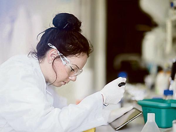 Eine junge Wissenschaftlerin pipettiert im Labor und hält dabei einen Tablett-Computer in der Hand.