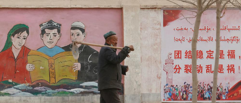Mandarin verdrängt Uigurisch. Ein Bauer in der Nähe von Kashgar in Xinjiang passiert propagandistische Wandbilder, die ethnische Minderheiten mit dem Slogan «Einheit, Stabilität ist Glück, Separatismus und Unruhe sind Unglück» dazu auffordern, die Verfassung ui lesen.