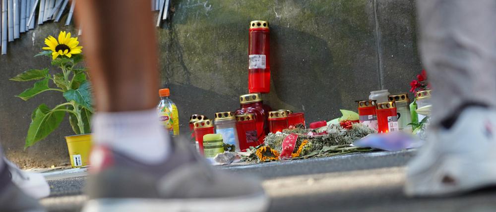 Menschen stehen vor einem Zaun, an dem mit Kerzen und Blumen eines von der Polizei erschossenen Jugendlichen gedacht wird. 