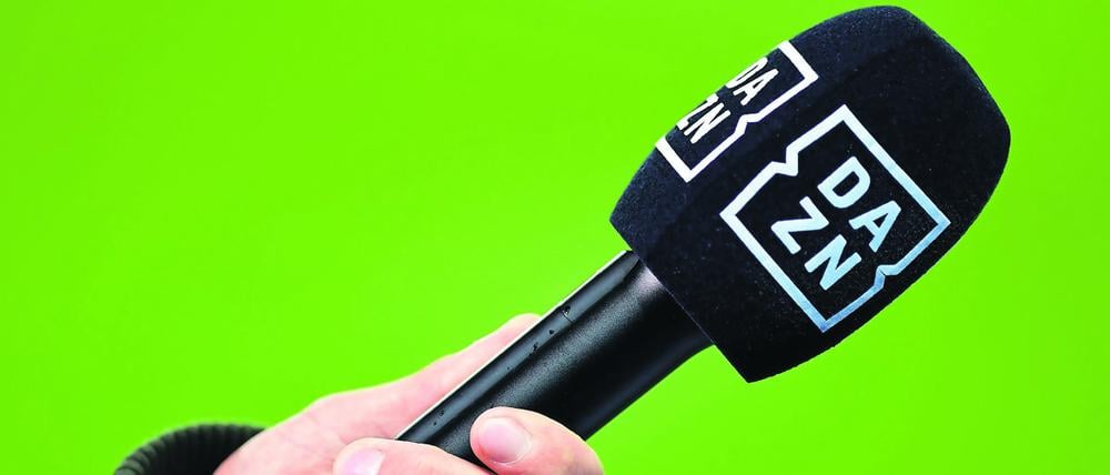 Ein Mikrofon des Kanals DAZN wird vor einen Greenscreen gehalten. (Symbolbild)