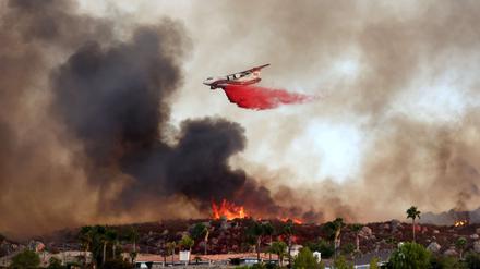 Ein Löschflugzeug wirft Löschmittel ab, während das Fairview-Feuer am 6. September 2022 in der Nähe von Häusern in Hanglage bei Hemet, Kalifornien, brennt.