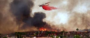 Ein Löschflugzeug wirft Löschmittel ab, während das Fairview-Feuer am 6. September 2022 in der Nähe von Häusern in Hanglage bei Hemet, Kalifornien, brennt.