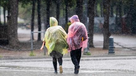 Passant:innen mit Plastik-Regenschutz gehen nahe des Brandenburger Tors durch den Regen. 