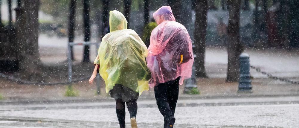 Passant:innen mit Plastik-Regenschutz gehen nahe des Brandenburger Tors durch den Regen. 
