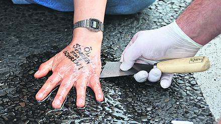 A police officer removes glue from the hand of a "Letzte Generation" (Last Generation) activist that reads "save oil instead of drill oil", blocking a road under the slogan "Let's stop the fossil madness!" for an end to fossil fuels and against oil drilling in the North Sea, in Berlin, Germany, July 15, 2022. REUTERS/Fabrizio Bensch