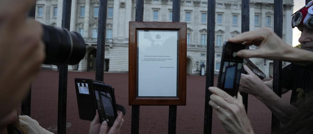 Menschen fotografieren die Bekanntgabe des Todes von Königin Elizabeth II., die an den Toren des Buckingham Palace hängt.