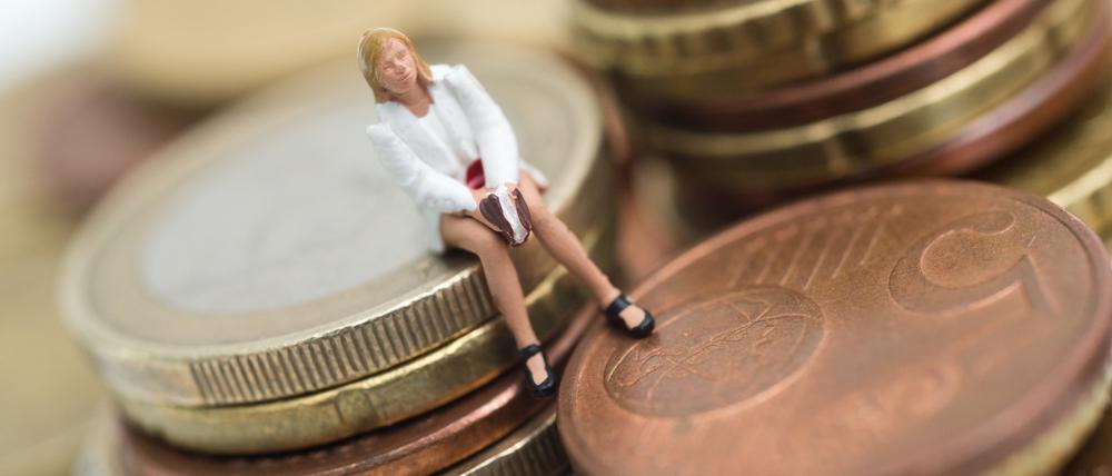 Eine kleine Plastilinfigur einer jungen Frau sitzt auf einem Stapel Geldstücke (Symbolfoto).