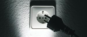 Ein schwarzer Stecker vor einer weißen Steckdose. (Symbolbild)