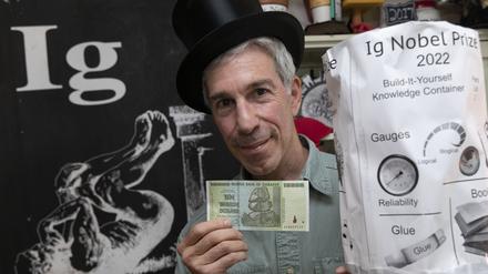 Zeremonienmeister Marc Abrahams hält einen 10-Billionen-Dollar-Schein und den Ig-Nobelpreis 2022 in seinem Büro. 