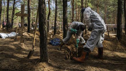 17.09.2022, Ukraine, Isjum: Zwei Arbeiter graben das Grab eines nicht identifizierten Zivilisten aus, zwischen anderen Gräbern ohne Namen von Zivilisten und ukrainischen Soldaten, während einer Exhumierung auf dem Waldfriedhof von Isjum, Ukraine. 