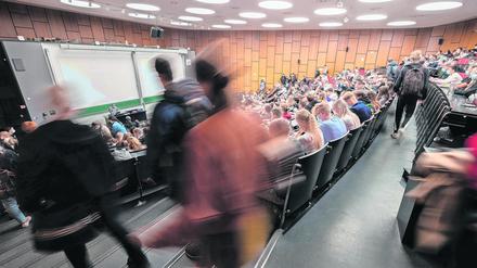 Studierende suchen sich in einem vollbesetzen Hörsaal einen freien Sitzplatz.