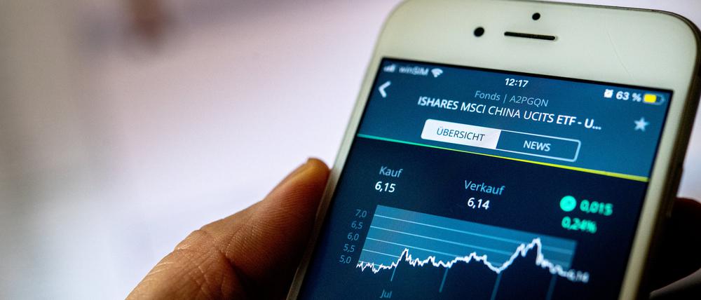 Eine Hand hält ein Smartphone, auf dessen Bildschirm ein Kursverlauf eines ETF auf chinesische Aktien zu sehen ist.