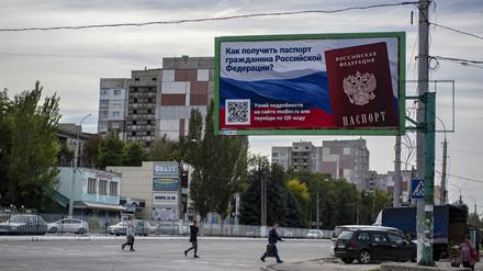 Menschen überqueren eine Straße mit einem Plakat mit der Aufschrift „Wie man den Pass eines russischen Bürgers bekommt“ vor dem Scheinreferendum in der von den von Russland unterstützten Separatisten kontrollierten Volksrepublik Luhansk in der Ostukraine. 