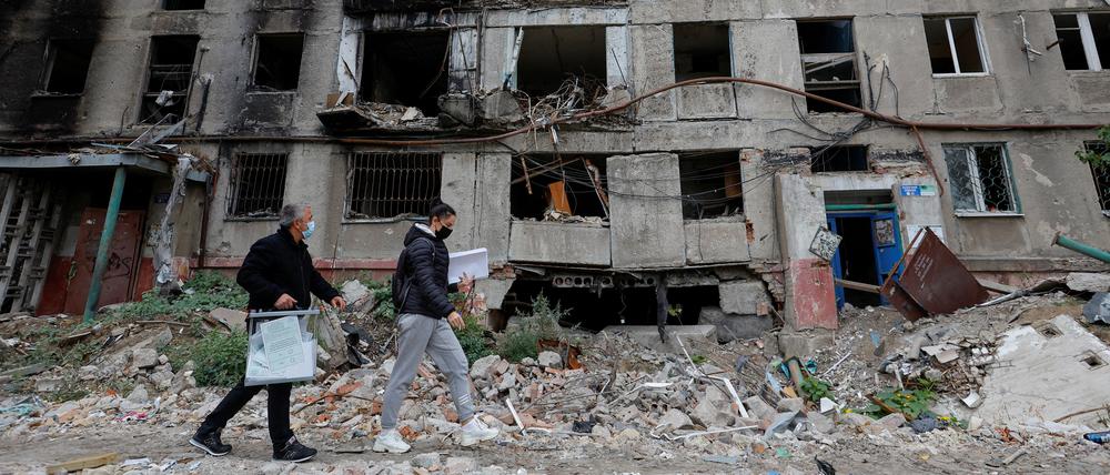 Mitglieder einer Wahlkommission laufen am 24. September vor einem zerstörten Gebäude in Mariupol vorbei.