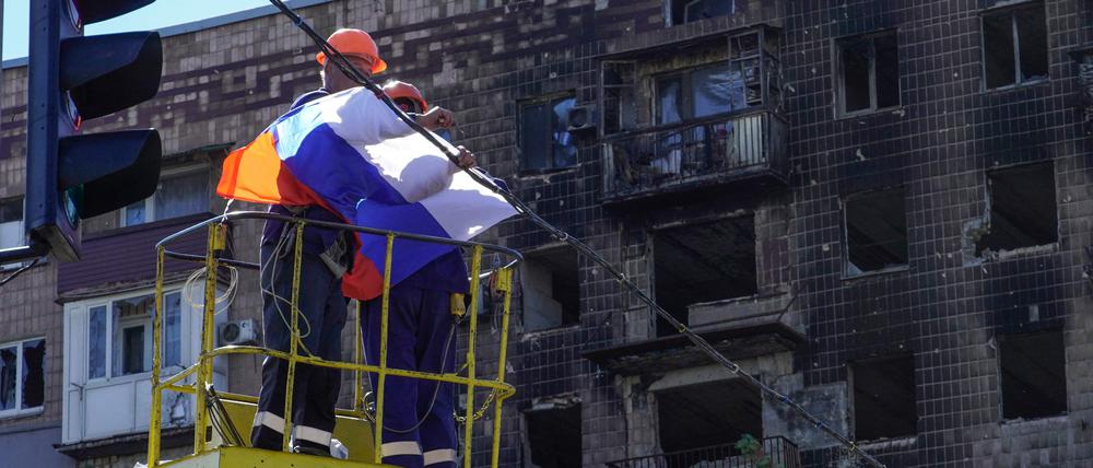 Ein Arbeiter befestigt eine russische Flagge in Mariupol.