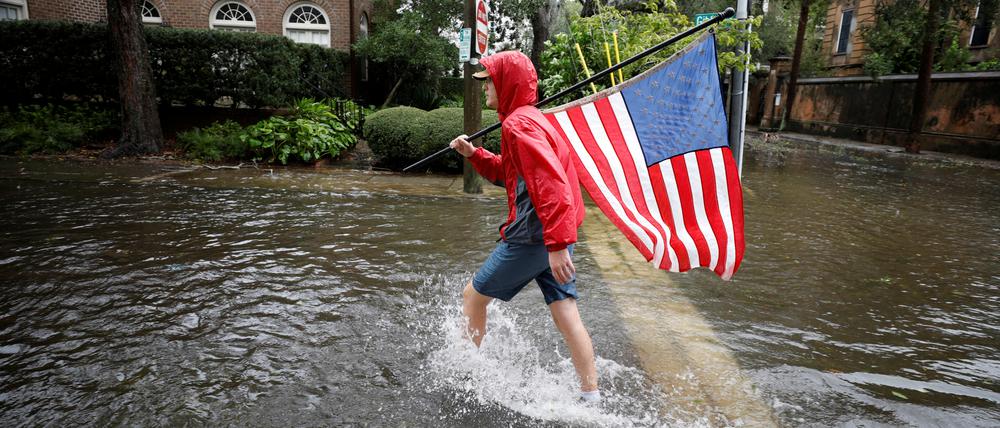Caden Simmons, ein 16-jähriger Anwohner, geht am 30. September 2022 mit einer US-Flagge auf einer überfluteten Straße spazieren.