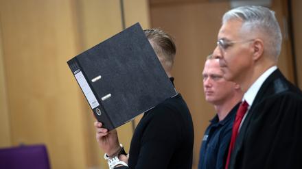 Der Angeklagte hält sich in einem Saal des Landgerichts Neuruppin (Brandenburg) einen Ordner vor das Gesicht. 
