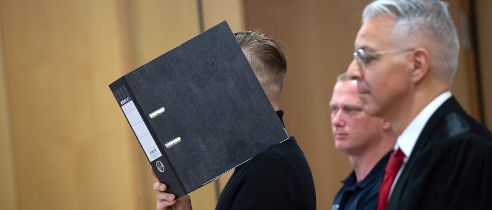 Der Angeklagte hält sich in einem Saal des Landgerichts Neuruppin (Brandenburg) einen Ordner vor das Gesicht. 