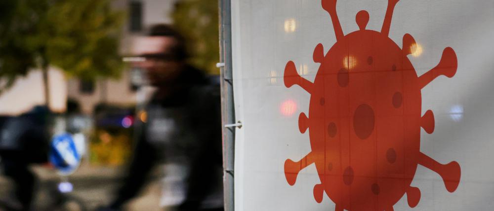 07.10.2022, Mecklenburg-Vorpommern, Rostock: Vor dem Hauptbahnhof weist ein großes Virus-Symbol auf die Corona-Teststation hin, die in Kürze öffnet, Radfahrer fahren daran vorbei. Foto: Bernd Wüstneck/dpa +++ dpa-Bildfunk +++