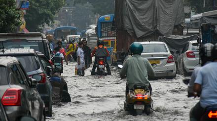 Indien, Kolkata: Menschen bahnen sich nach heftigen Regenfällen zu Fuß, in ihren Autos und auf Mopeds den Weg über eine überflutete Straße der Stadt.