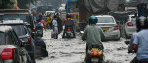 Indien, Kolkata: Menschen bahnen sich nach heftigen Regenfällen zu Fuß, in ihren Autos und auf Mopeds den Weg über eine überflutete Straße der Stadt.