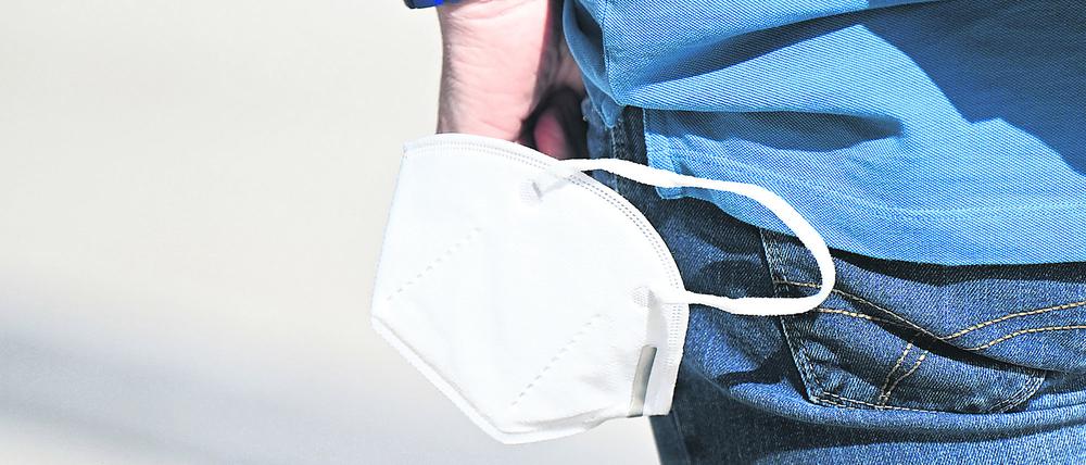 Ein Mann trägt an seinem Handgelenk eine Schutzmaske. Brandenburgs Landesregierung ist uneins über die Maskenpflicht.