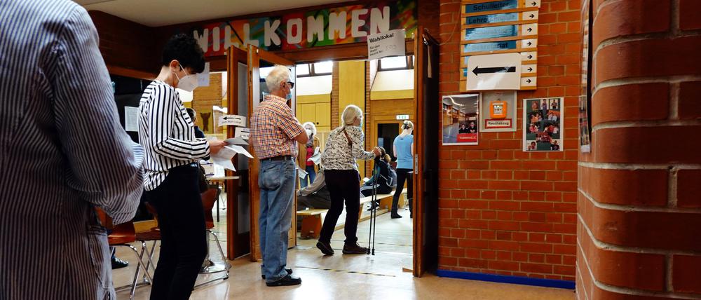 Menschen stehen vor einem Wahllokal in einer Berliner Schule an. 