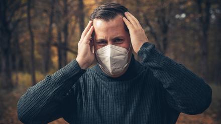 Ein kranker Mann steht mit FFP2-Maske aus unbekanntem Grund im Wald.