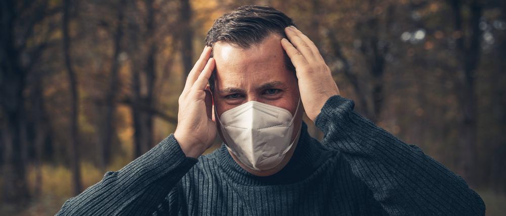 Ein kranker Mann steht mit FFP2-Maske aus unbekanntem Grund im Wald.