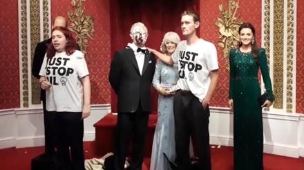 Zwei Aktivisten neben der mit Schokoladenkuchen beschmierten Wachsfigur von König Charles III.
