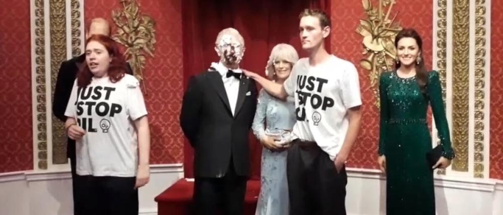 Zwei Aktivisten neben der mit Schokoladenkuchen beschmierten Wachsfigur von König Charles III.