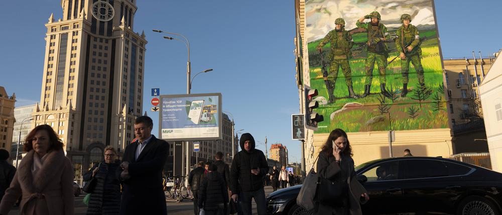 Vor dem Hintergrund einer Militärmalerei an einer Hauswand machen sich die Menschen in Moskaus Stadtzentrum auf den Weg in die Arbeit.