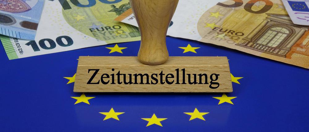 Vor Geldscheinen steht ein Stempel mit dem Schriftzug „Zeitumstellung“.