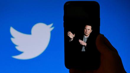 Ein Foto von Elon Musik auf einem Telefondisplay mit dem Twitter-Logo im Hintergrund.