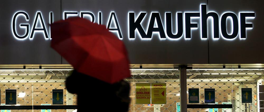 Eine Frau geht mit Regenschirm an einer geschlossenen Kaufhof Filiale vorbei.