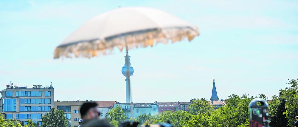 05.06.2022, Berlin: Ein Mann liegt im Mauerpark vor dem Berliner Fernsehturm unter einem Sonnenschirm. Foto: Christoph Soeder/dpa +++ dpa-Bildfunk +++