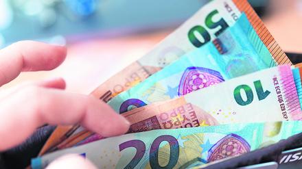 Eine Frau hält ein Portemonnaie in der Hand, in dem Geldscheine stecken. 