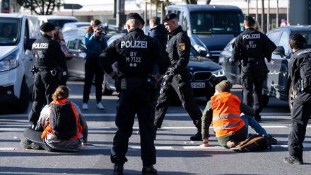Polizeibeamte stehen neben Klimaaktivisten, die sich am Karlsplatz in der Innenstadt auf die Fahrbahn geklebt und somit die Straße blockiert haben. 