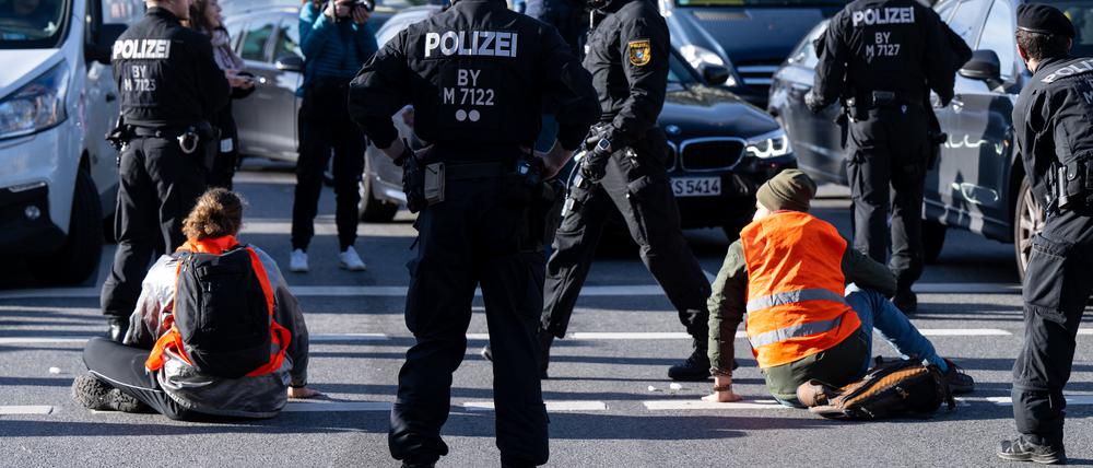 Polizeibeamte stehen neben Klimaaktivisten, die sich am Karlsplatz in der Innenstadt auf die Fahrbahn geklebt und somit die Straße blockiert haben. 