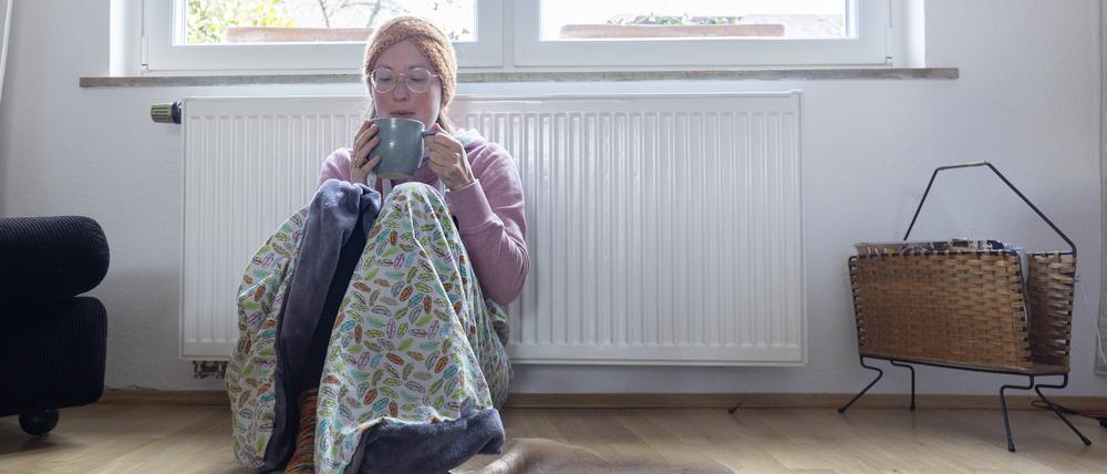 Eine Frau sitzt in einer Decke vor einem Heizkörper.