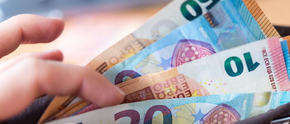 Eine Frau hält ein Portemonnaie in der Hand, in dem Geldscheine stecken.
