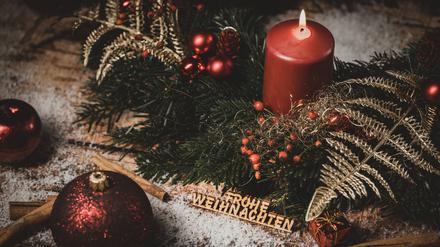 Adventskranz-Kerze und Holz-Aufschrift: Frohe Weihnachten.