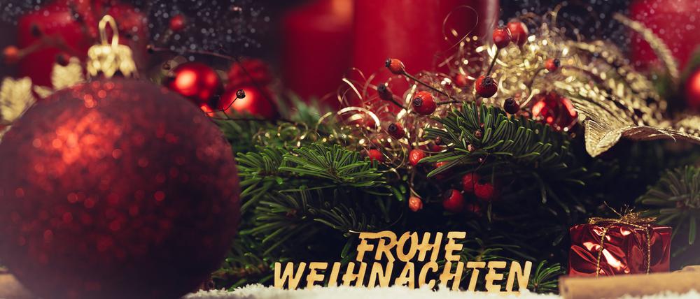 Adventskranz mit brennender Kerze und einer Holzschrift: Frohe Weihnachten.